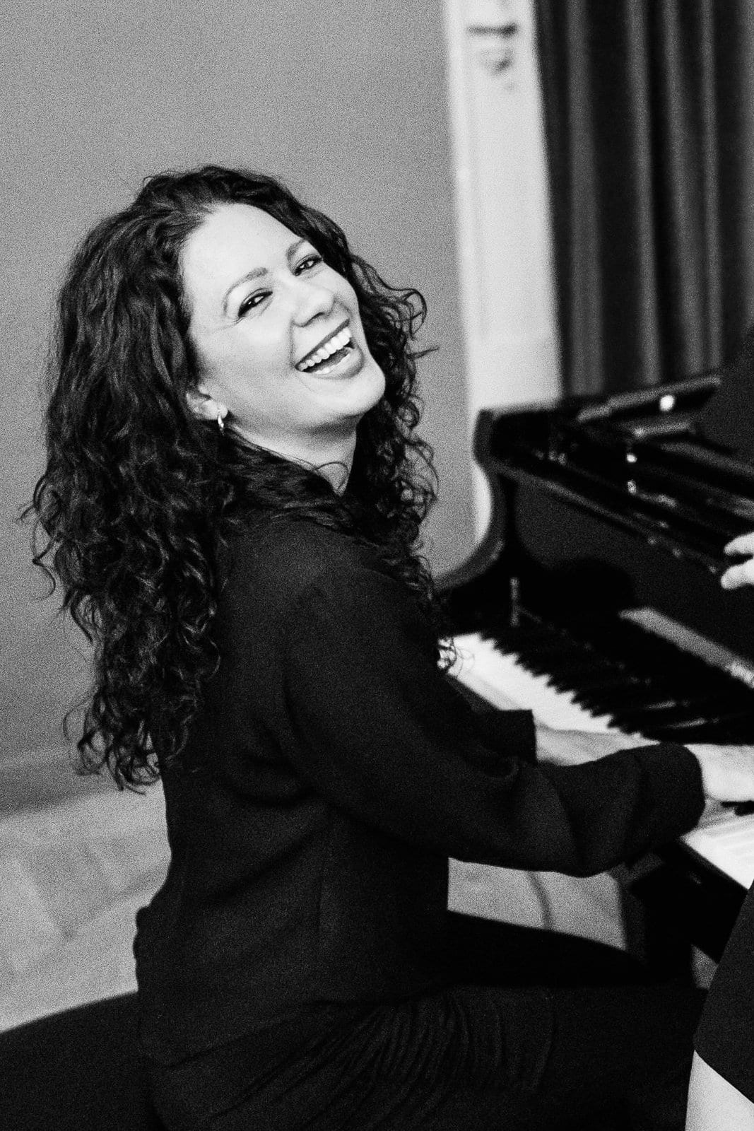 Joanna González sonriendo al piano, blanco y negro